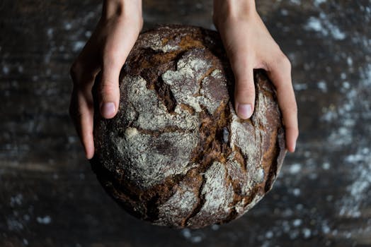 Close-up of hands holding a rustic loaf of whole wheat bread with a dark, textured crust.
