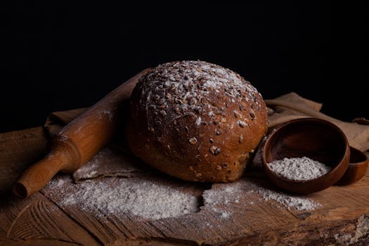 Rustic loaf of fresh seeded bread with flour in a dark, moody setting.