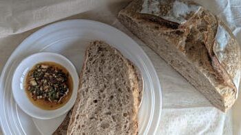 Rustic sourdough bread served with a herbed oil dip on a white plate.
