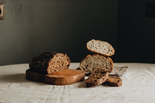Slices of tasty freshly baked sourdough bread placed on crumpled tablecloth on table with cutting board in light room on black background
